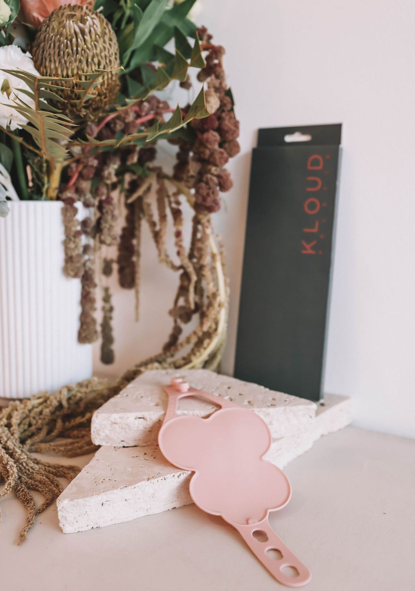 Kloud Palette's sleek black packaging stands upright beside a blush pink hand palette, styled with dried florals and textured stone—emphasizing the product’s modern, eco-conscious aesthetic. Designed for professional makeup artists seeking hygienic, skin-safe mixing tools with visual appeal.