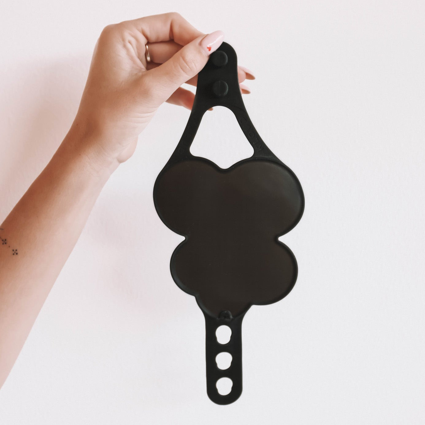 Hand holding the black Kloud Palette against a white background, showing its cloud-shaped design and adjustable wrist strap. This latex-free, professional makeup tool is made from premium, skin-safe materials for hygienic and efficient product mixing.