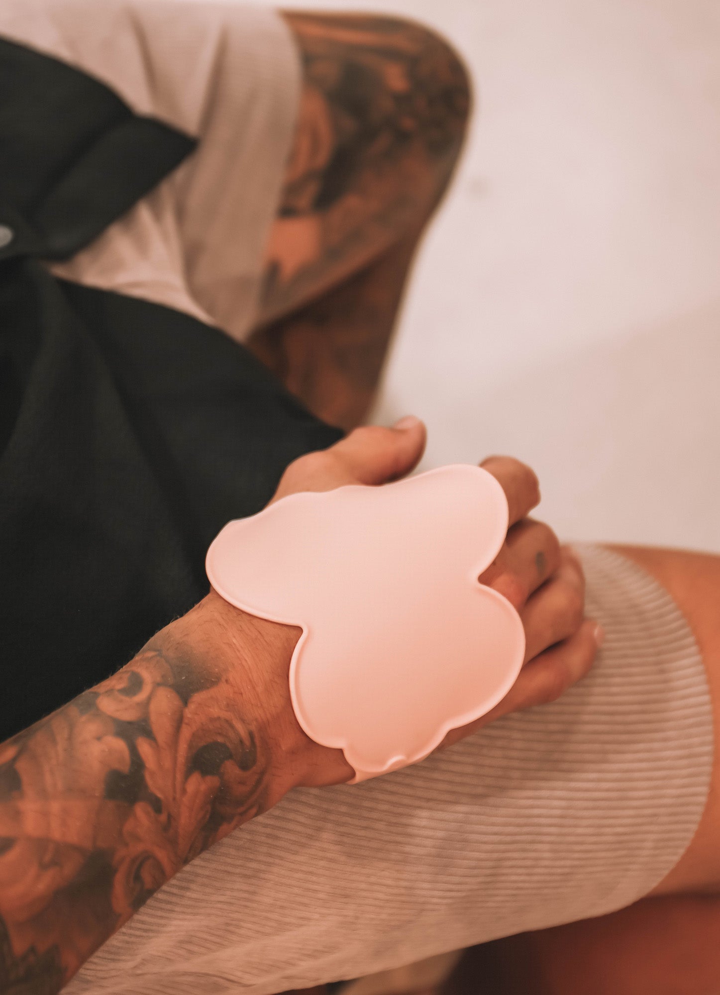 Close-up of a tattooed arm wearing the blush pink Kloud Palette, a cloud-shaped wrist tool crafted for beauty professionals. Made from premium, skin-safe silicone, this latex-free palette offers a durable, comfortable surface for hygienic colour mixing and all-day wear.