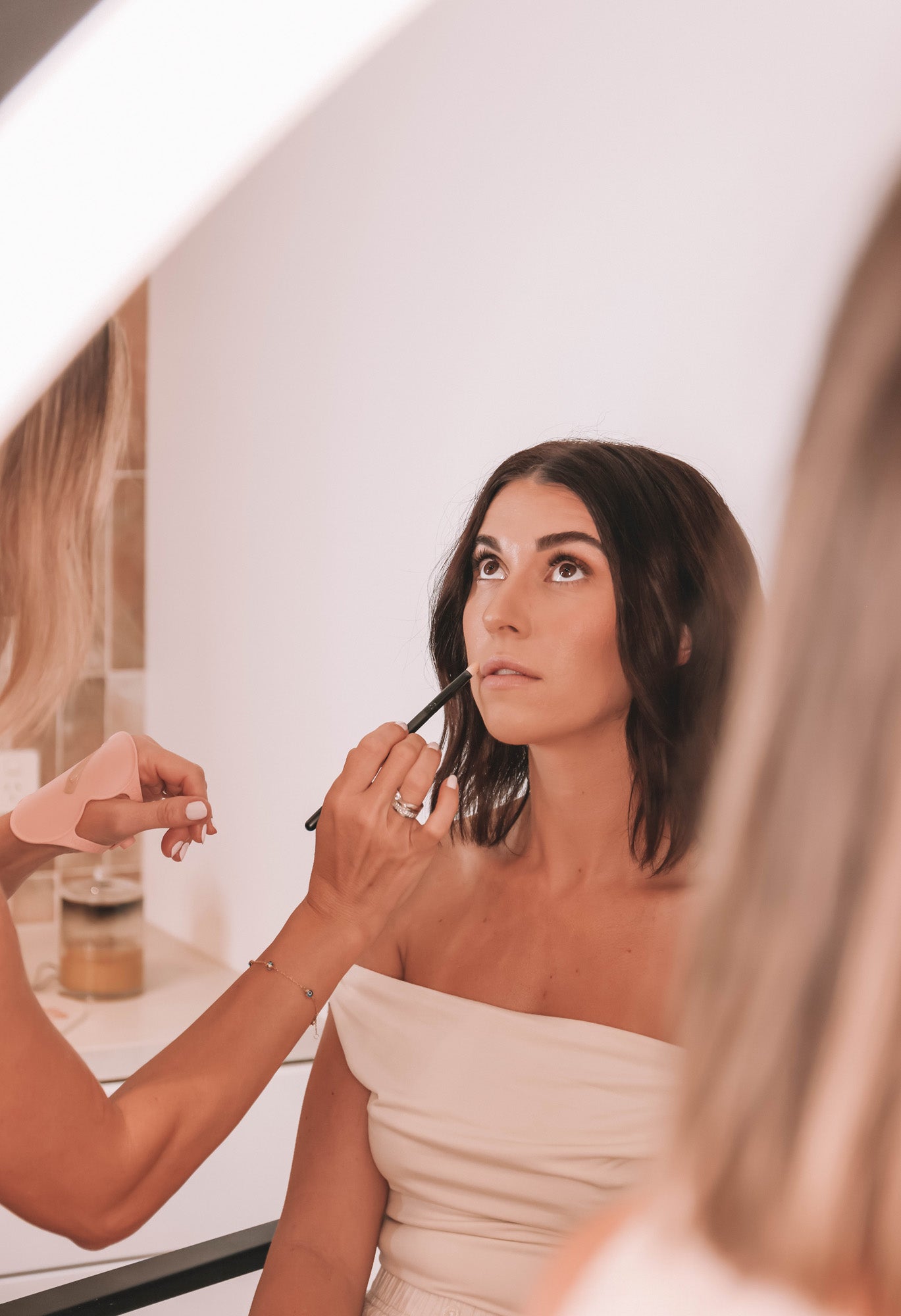 A beauty professional applies lip to a client while wearing a blush pink Kloud Palette on her wrist, using it to hold product during the session. Crafted from premium, skin-safe materials, this latex-free, cloud-shaped tool is designed to enhance artistry while minimising contact and allergic reactions.