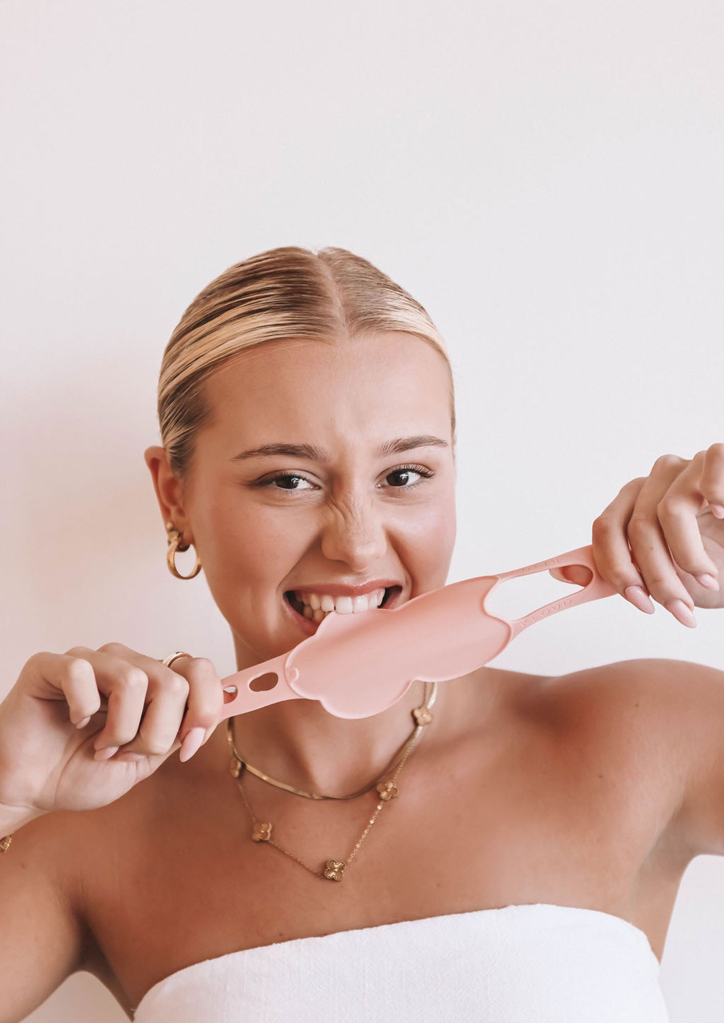 Smiling woman playfully biting a pink Kloud Palette, a cloud-shaped beauty tool designed for hygienic and seamless mixing of cosmetic colors. Ideal for beauty professionals seeking innovative, allergy-conscious tools.
