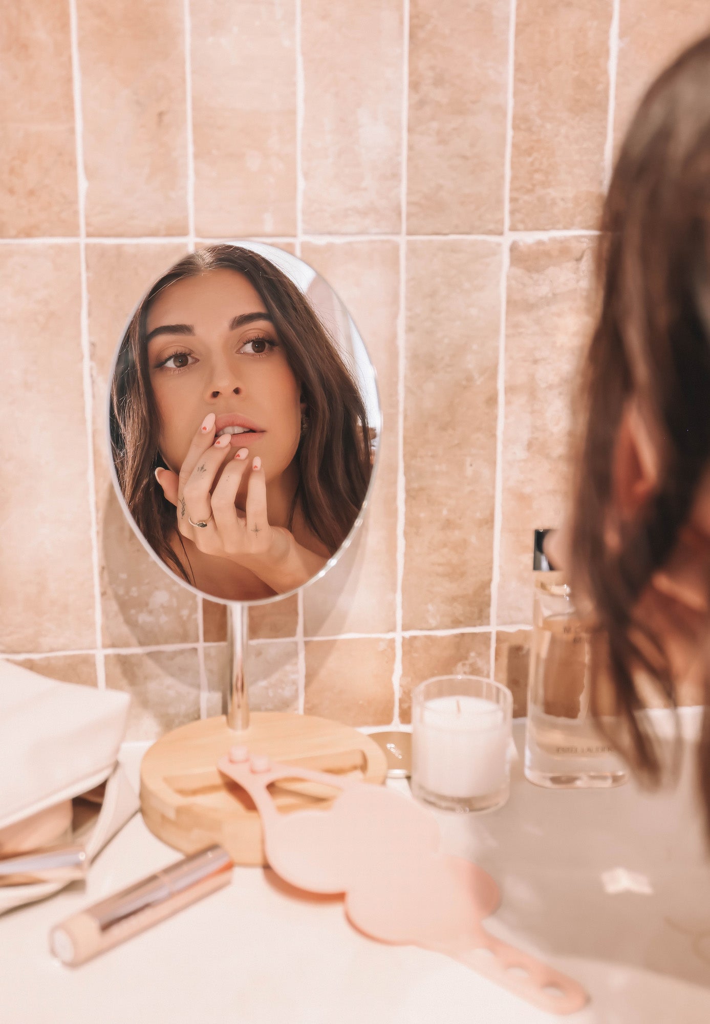 Woman applying makeup in the mirror at a tiled vanity, with a blush pink Kloud Palette placed beside a candle and beauty tools. The latex-free, cloud-shaped palette blends into a calm, professional setting—ideal for beauty pros who value aesthetics, hygiene, and efficiency.